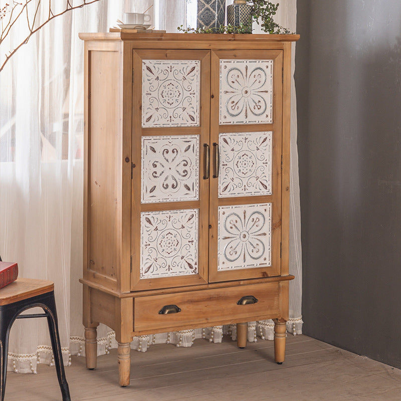 The Rustic Sideboard and Wall Shelf Set by Furnishaus exudes charm with double doors featuring ornate white carved panels in floral and geometric patterns, centered by a drawer with metal handles. Topped with greenery, sheer curtains, and a dark wall enhance the decorative aesthetic.